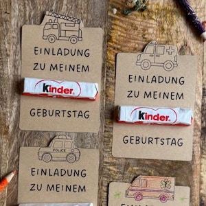 May include: A wooden display featuring invitation cards with emergency vehicle illustrations. Each card includes the text "EINLADUNG ZU MEINEM GEBURTSTAG" and a Kinder chocolate bar. Colored pencils are scattered around the cards.