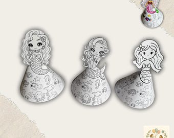 Puede incluir: Tres figuras blancas de sirenas para manualidades con detallados dibujos lineales, listas para colorear. Las sirenas tienen el pelo suelto y están adornadas con diseños de conchas marinas y estrellas de mar. El texto "Basteln mit Kinder" está en la parte superior.