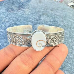 Op de afbeelding: Zilveren manchetarmband met een ovale, crèmekleurige middenstuk met een spiraalvormig ontwerp. De armband heeft bloemen- en paisley-patronen. De tekst "VKJEWELLERSCreations" is zichtbaar.