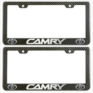 Pode incluir: Duas molduras pretas para chapas de matrícula em fibra de carbono. Cada moldura tem a palavra "CAMRY" em letras prateadas, juntamente com o logótipo da Toyota. As molduras têm um padrão texturizado e orifícios de montagem.