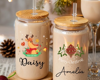 May include: Two glass beverage containers with wooden lids and clear straws. One features a reindeer graphic and the name "Daisy", the other has a Christmas ornament design and the name "Amelia". Both are filled with a light-colored beverage.