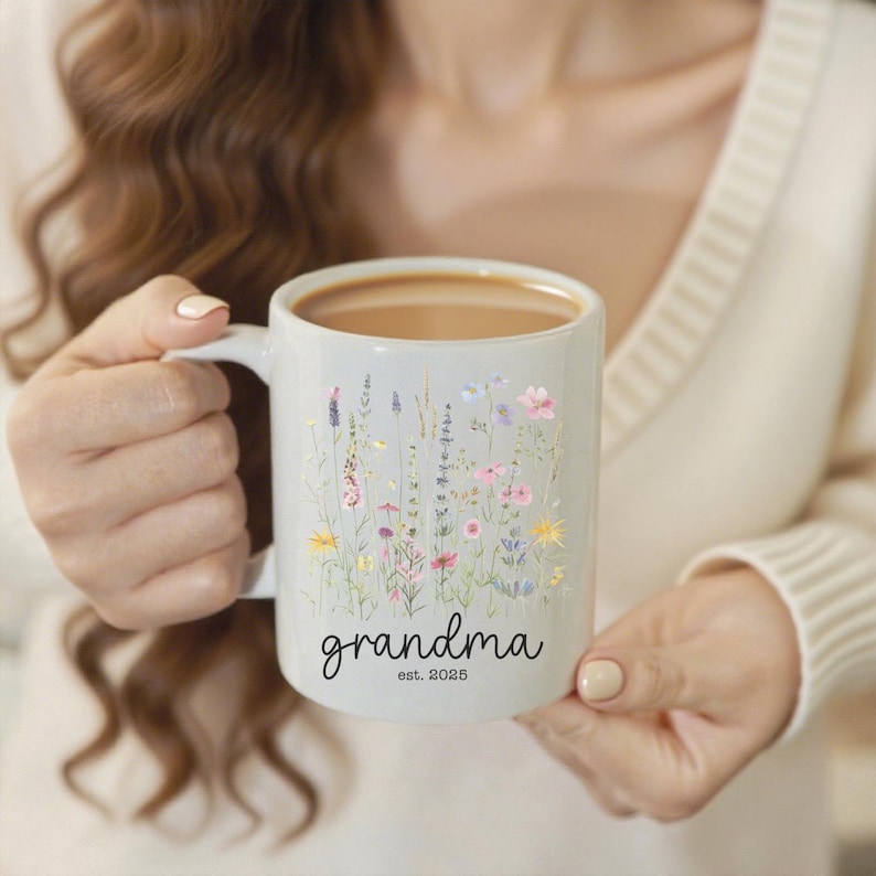 Puede incluir: Taza de cer&aacute;mica blanca con un dise&ntilde;o floral y la palabra "grandma" en escritura cursiva. La taza tambi&eacute;n incluye el texto "est. 2025". La taza est&aacute; llena de un l&iacute;quido marr&oacute;n.