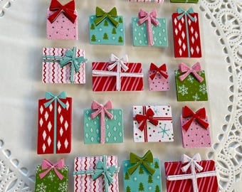 May include: A selection of small, decorative gift boxes in assorted colours and patterns. Designs include snowflakes, Christmas trees, and zigzags. Bow colours include red, pink, and green. The gifts are arranged on a white, lacy doily.