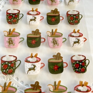 May include: A sheet of 20 festive Christmas-themed stickers featuring mugs of hot chocolate with various toppings, including marshmallows, gingerbread men, cinnamon sticks, and a lemon wedge. The mugs are decorated with different patterns, including red and green floral designs, a white reindeer, and a red poinsettia.