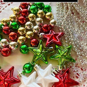 May include: A collection of miniature Christmas ornaments, including red, green, gold, and silver bells, star-shaped ornaments in red, green, and white, and a strand of silver beads. The word "MINIATURE" is displayed in a black rectangle at the top.