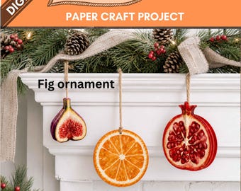 May include: A digital printable paper craft project featuring three hanging fruit ornaments: a sliced fig, a sliced orange, and a sliced pomegranate. Each ornament is suspended by a twine string. The text "DIGITAL PRINTABLE 3-D PNG / PDF PAPER CRAFT PROJECT" and "Fig ornament" are visible.