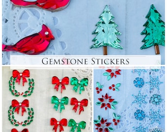 Puede incluir: Surtido de pegatinas de piedras preciosas con temática navideña. Las pegatinas presentan coronas, lazos, copos de nieve y árboles de Navidad. El texto "GEMSTONE STICKERS" está impreso en la imagen.
