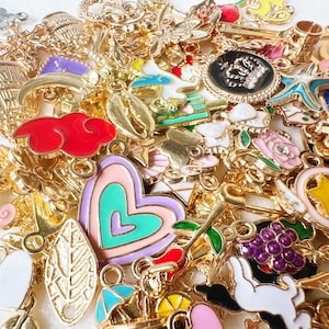 Könnte beinhalten: Eine Sammlung goldfarbener Charms mit farbenfrohen Emaille-Details. Die Charms umfassen verschiedene Formen wie Herzen, Blätter, Wolken und Sterne. Einige Charms weisen florale und tierische Designs auf, mit einer Vielzahl von Farben wie Rot, Rosa, Blau und Lila.