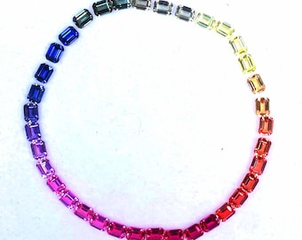 May include: A collection of rectangular gemstones arranged in a circular pattern, showcasing a gradient of colors. The gemstones transition from deep blues and purples to vibrant pinks, reds, oranges, yellows, and greens, creating a rainbow effect.