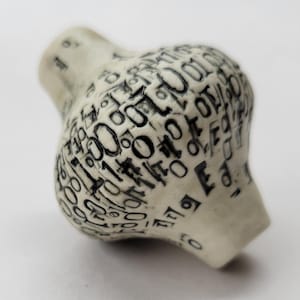 May include: A spherical, off-white ceramic bead featuring a textured surface covered in black, debossed binary code digits including ones and zeros. The bead has a slightly tapered, cylindrical opening at the top and bottom, creating a rounded shape.