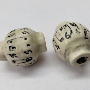 Puede incluir: Dos pomos de cerámica blanquecina con notación musical negra. Los pomos tienen forma redondeada con base cilíndrica, probablemente para un armario o cajón. Las notas musicales incluyen números y símbolos.