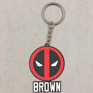 May include: A keychain with a black and red graphic design featuring white eye shapes and the word "BROWN" in white block letters. The keychain has a silver-colored ring and chain.