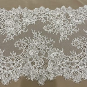 以下が含まれることがあります： スカラップエッジの白いフローラルレーストリム。レースは、花と葉の細かいパターンが特徴です。繊細な生地はニュートラルな背景に配置され、複雑なデザインを際立たせています。縫製やクラフトプロジェクトに最適です。