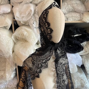 Wide black floral lace trim with double scalloped edges, sold as a 3m piece. Features an intricate floral pattern with oval medallions on a soft, sheer mesh base. Made from a blend of polyester and nylon, this lace is ideal for wedding veils, evening dresses, shawls, lingerie, and sewing projects. The double scalloped edges allow use without additional finishing, making it perfect for both beginners and professional designers.