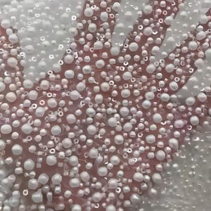 May include: Close-up of a pink surface covered in white, pearl-like beads. The beads vary in size and density, creating a textured, three-dimensional effect. The image suggests a decorative or craft element.