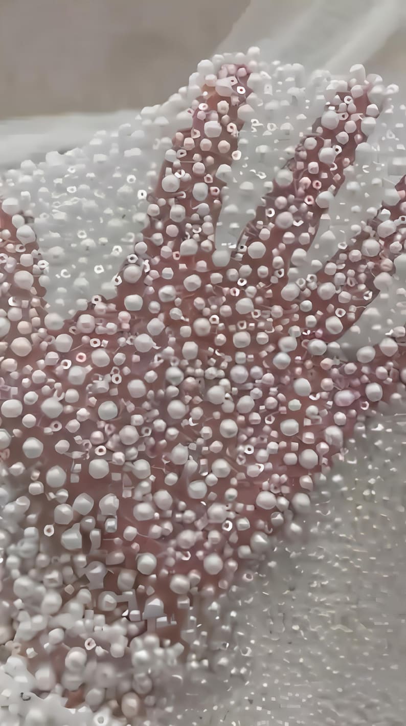 May include: Close-up of a pink surface covered in white, pearl-like beads. The beads vary in size and density, creating a textured, three-dimensional effect. The image suggests a decorative or craft element.