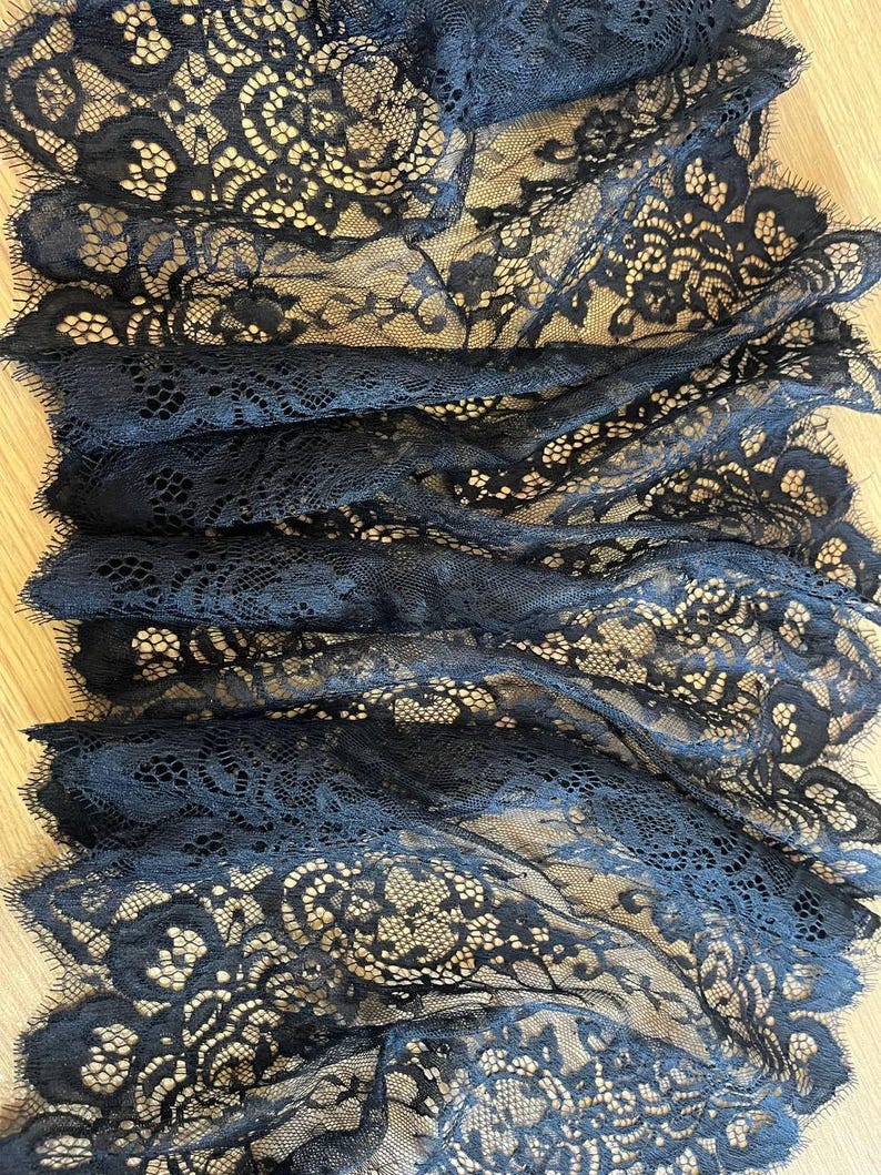 Peut inclure: Gros plan sur un tissu en dentelle noire avec des motifs floraux complexes. La dentelle est superpos&eacute;e, cr&eacute;ant un effet textur&eacute;. Le design d&eacute;licat et la couleur sombre sugg&egrave;rent une utilisation formelle ou d&eacute;corative, peut-&ecirc;tre pour l'habillement ou l'artisanat.
