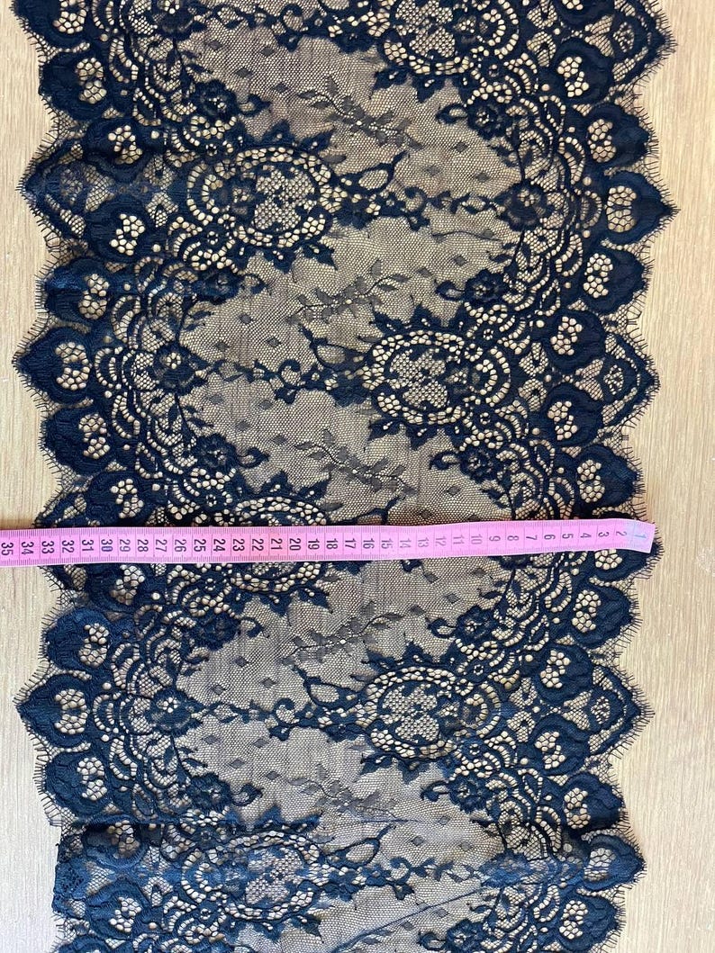 Peut inclure: Tissu en dentelle bleu marine avec un motif floral et des bords festonn&eacute;s. Un ruban &agrave; mesurer rose indique la longueur du tissu. Le tissu mesure environ 89 cm de long.