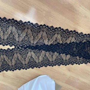 Peut inclure: Deux morceaux de tissu en dentelle noire avec un motif floral. La dentelle a un bord festonn&eacute; et est pos&eacute;e sur une surface en bois. Le tissu est probablement utilis&eacute; pour des projets de couture ou d'artisanat.