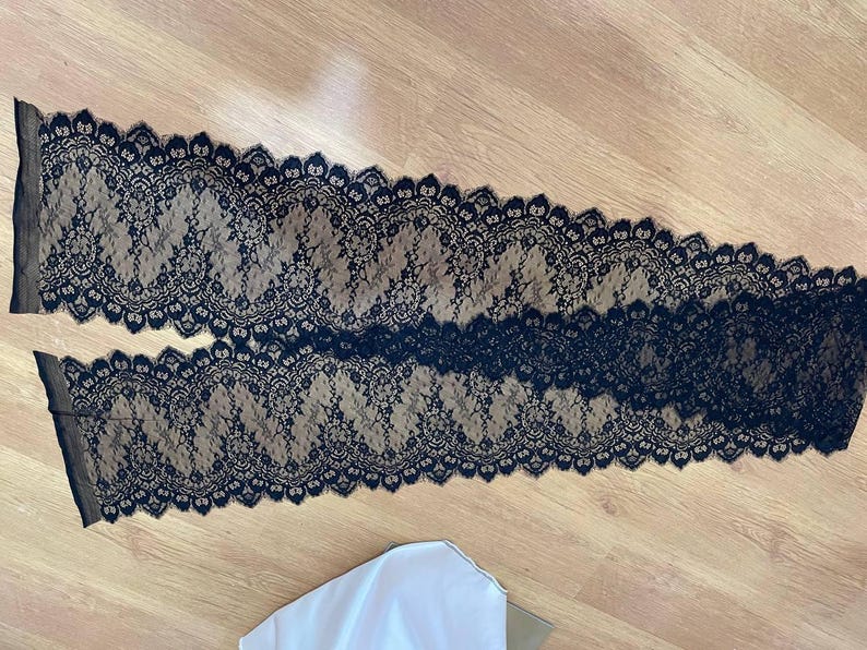 Peut inclure: Deux morceaux de tissu en dentelle noire avec un motif floral. La dentelle a un bord festonn&eacute; et est pos&eacute;e sur une surface en bois. Le tissu est probablement utilis&eacute; pour des projets de couture ou d'artisanat.