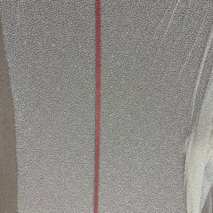 May include: A large piece of white fabric with a dense pattern of small, raised dots. A red measuring tape runs vertically down the center, indicating length. The fabric appears to be a decorative textile, possibly for apparel or crafts.