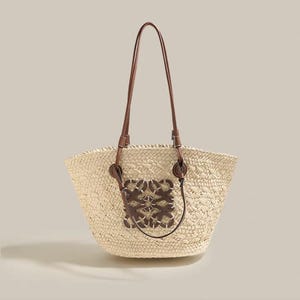 Peut inclure: Un sac fourre-tout en paille tressée avec des anses et des détails en cuir marron. Le sac présente un patch décoratif en cuir marron sur le devant. Il a une large ouverture et une forme structurée.