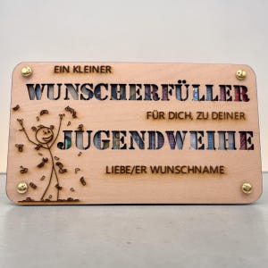 May include: A light-colored wooden plaque with cut-out lettering and a stick figure celebrating with money. The text includes "EIN KLEINER WUNSCHERF&Uuml;LLER" and "JUGENDWEIHE". Gold-colored screws secure the corners.