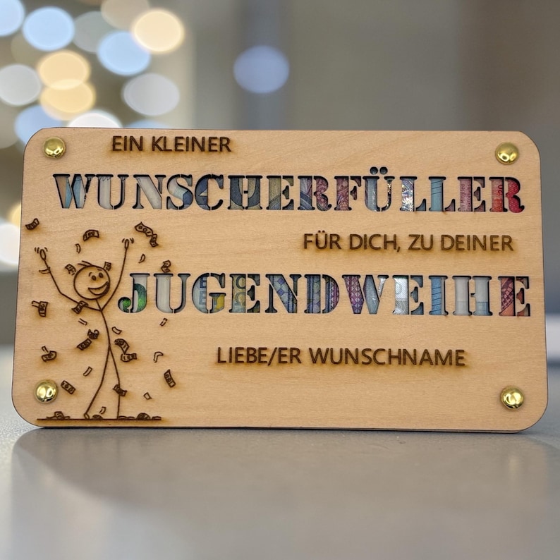 May include: A wooden plaque with the words "EIN KLEINER WUNSCHERF&Uuml;LLER F&Uuml;R DICH, ZU DEINER JUGENDWEIHE" and "LIEBE/ER WUNSCHNAME" engraved. The letters are filled with colorful designs. A stick figure is drawn on the left.