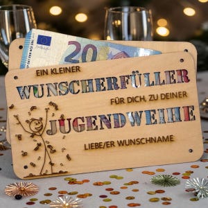 May include: A wooden gift card holder with the text "EIN KLEINER WUNSCHERF&Uuml;LLER F&Uuml;R DICH, ZU DEINER JUGENDWEIHE" and a stick figure. The holder contains a 20 Euro bill. Confetti is scattered around the holder.