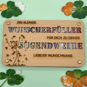 May include: A wooden plaque with the words "EIN KLEINER WUNSCHERF&Uuml;LLER F&Uuml;R DICH, ZU DEINER JUGENDWEIHE" engraved on it. The word "JUGENDWEIHE" is filled with colorful paper money. A stick figure is celebrating with money falling around it.