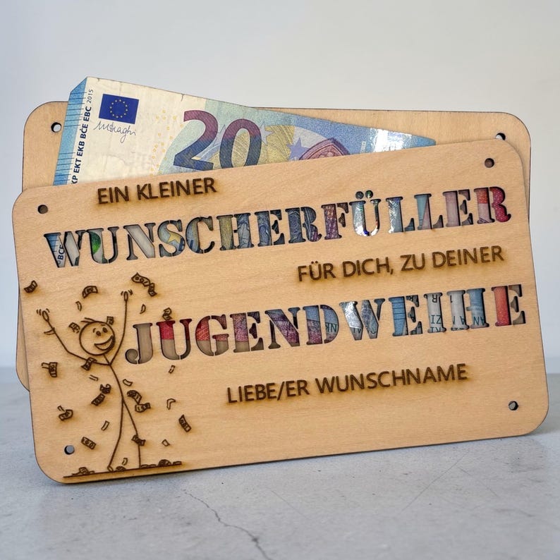 May include: A wooden gift card holder with a cutout design. The holder has the words "EIN KLEINER WUNSCHERF&Uuml;LLER F&Uuml;R DICH, ZU DEINER JUGENDWEIHE" and a stick figure. A twenty-dollar bill is visible inside the holder.
