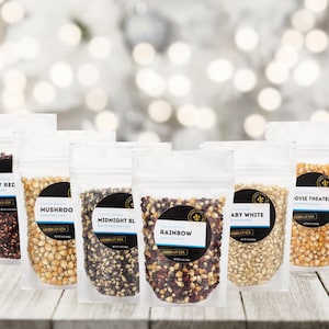 May include: Seven bags of popcorn kernels, each with a different color and variety. The bags are labeled with the names "Ruby Red", "Mushroo", "Midnight BL", "Rainbow", "Aby White", "Movie Theater", and "Popcorn Kernels".