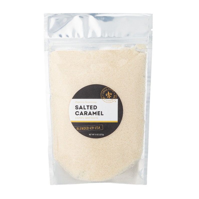 May include: A silver resealable pouch filled with a light brown seasoning blend. The label reads "Grill Cove Seasoning, Salted Caramel, a buttery, sweet savory, Blended in the USA, Net Wt: 8 oz (227g)"