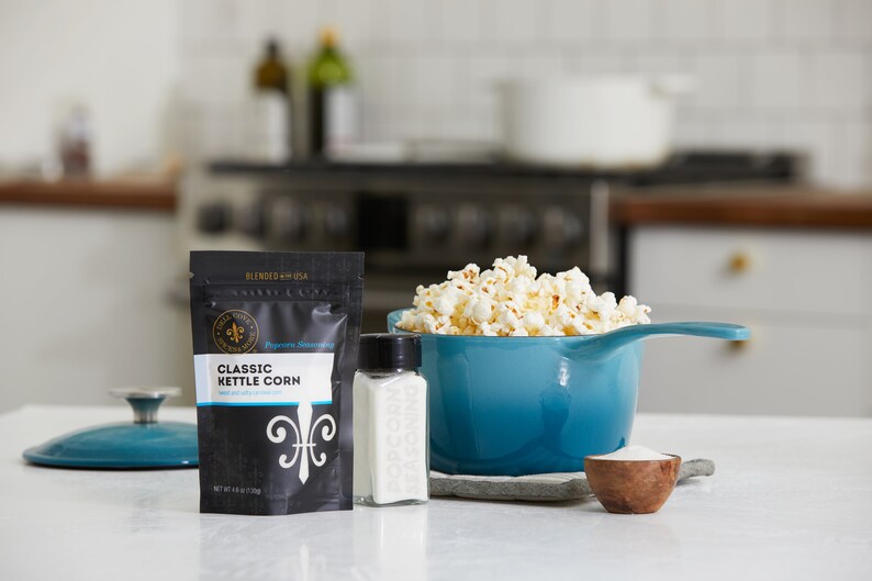 Blue kettle on counter next to classic kettle corn seasoning pouch, small wooden bowl filled with seasoning and glass shaker filled with seasoning. Dell Cove Spices