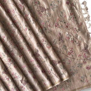 May include: Beige fabric featuring embroidered birds and floral branches. The fabric has vertical stripes and is decorated with pink and green floral accents. Tassels are visible on the edge.