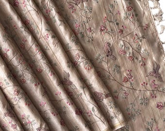 Puede incluir: Tela beige con bordados de pájaros y ramas florales. La tela tiene rayas verticales y está adornada con detalles florales rosas y verdes. Se ven borlas en el borde.