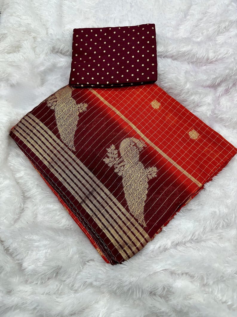 May include: A red and maroon saree with gold accents and bird motifs. The saree has a checkered pattern and striped border. A maroon blouse piece with gold polka dots is included.
