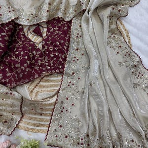 Peut inclure: Ensemble élégant composé d'un haut bordeaux orné de broderies dorées et d'un châle crème scintillant. Le châle est orné de sequins argentés et d'accents rouges, créant un look luxueux. Idéal pour les occasions spéciales.