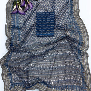 May include: A blue patterned fabric set with a matching top. The fabric is draped, showcasing a detailed design with small mirrors and floral accents. Purple flowers are placed on the top left corner.