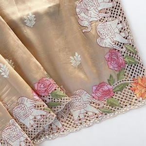 May include: Beige fabric with embroidered details. The border features white elephants, pink roses, and orange flowers. The fabric has a delicate, sheer quality with small embroidered leaf accents.