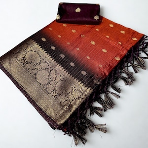 May include: A vibrant orange and black ombre saree with gold floral detailing and a matching burgundy fabric piece. The saree features a decorative border with intricate gold patterns and a fringed edge.