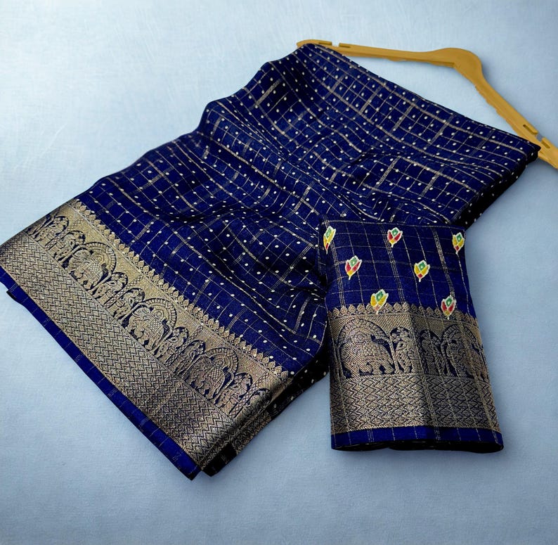 Op de afbeelding: Een marineblauwe sari met een goud-wit rasterpatroon. De sari heeft een decoratieve gouden rand met olifantenmotieven. Een bijpassend marineblauw stuk stof met een vergelijkbare rand is ook inbegrepen.