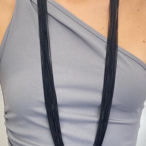 May include: A long multi-strand necklace composed of numerous thin, black metallic chains that drape vertically from the neck, creating a layered, uniform appearance with a consistent dark color throughout the entire length of the accessory.