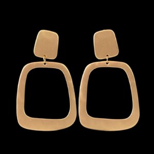 May include: A pair of gold-coloured earrings with a geometric design. Each earring features a small, square top piece connected to a larger, open square shape below. The earrings have a matte finish and hang from a small loop.
