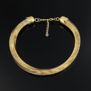 Puede incluir: Un collar tipo gargantilla de tono dorado con un diseño de cadena de serpiente flexible y acanalada. El collar está rematado con extremos redondeados y lisos, e incluye una delicada cadena extensora ajustable con cierre de mosquetón.