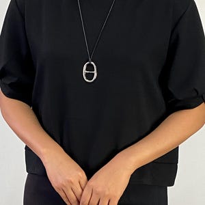 Modernt ovalt silverhalsband med hänge – skulpturalt minimalistiskt uttalande på svart snöre