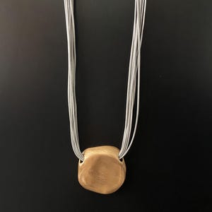Modern Artisan Pendant Necklace – Brushed Matte Gold Pebble Charm on Multi-Strand Grey Cord