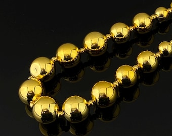 May include: A necklace composed of polished, reflective gold-colored spherical beads strung together in a continuous line. The beads are uniform in shape and size, creating a smooth, metallic appearance that catches the light across their curved surfaces.
