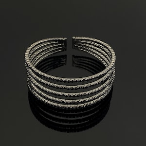 May include: A gunmetal-toned cuff bracelet featuring five parallel rows of small, square-cut dark stones. The bracelet has an open-ended design, allowing for adjustment, and displays a uniform, metallic finish across all five connected bands.