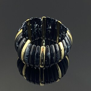 May include: A stretch bracelet featuring alternating vertical segments of black and white marbled resin and polished gold-tone metal. The cylindrical pieces are arranged in a continuous circular band, creating a high-contrast, reflective accessory.